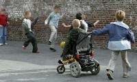 En gruppe af skolebørn spiller bold i skolegården. Et af børnene er i kørestol.