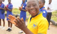 En dreng med udviklingshæmning klapper og smiler med ghanesiske spejdere i baggrunden