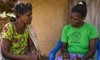 To ugandiske kvinder sidder og taler sammen foran et hus.